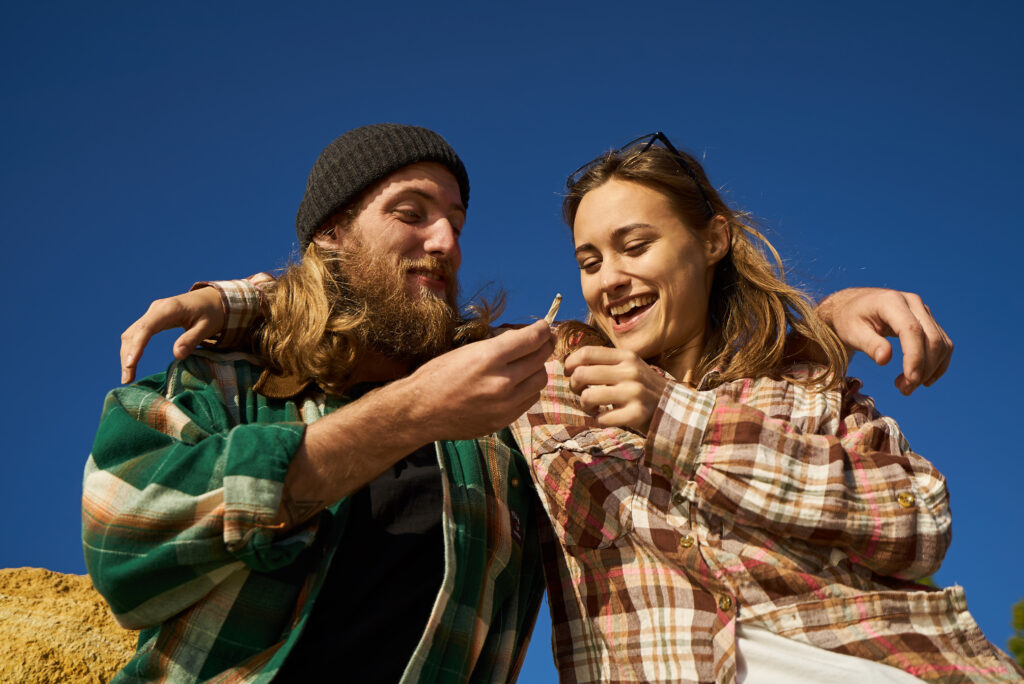 couple of cheerful hipster friends passing joint outdoors on a sunny day